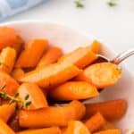 Closeup of a bowl of honey roasted carrots with a spoon in it.