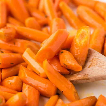 Baked carrots being scooped from a pan with a wooden spoon