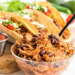 shredded chicken with black beans in a bowl with tacos in the background