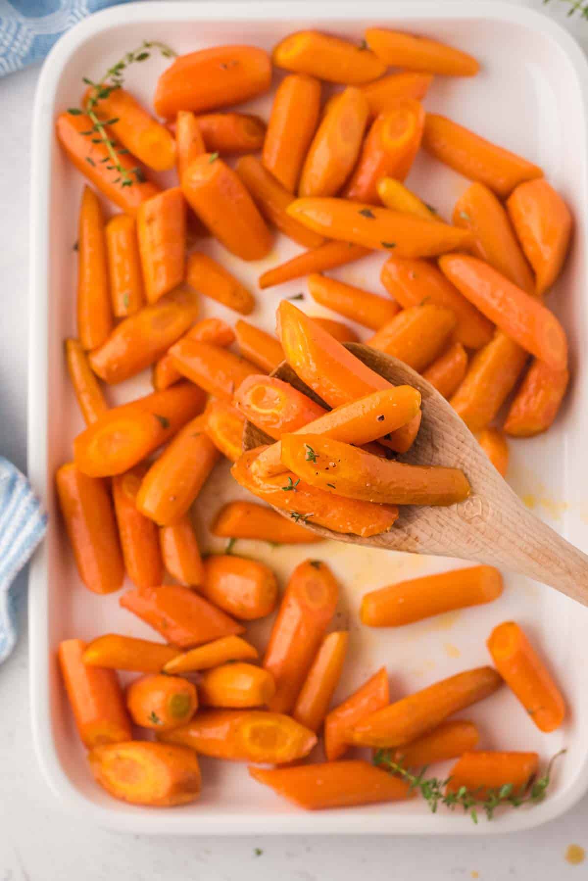 Roasted carrots scooped from a baking dish with a wooden spoon