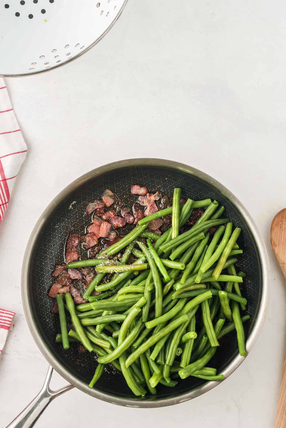 Adding green beans to bacon cooked in a skillet.