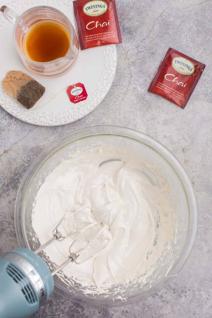 Brewed chai tea next to a bowl of chai royal icing being blended with a hand mixer