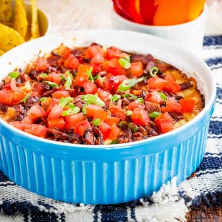 Hot dip in a casserole with bowls of bell pepper slices and tortilla chips