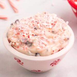 Peppermint cheesecake dip in a white bowl with peppermint candy graphics on it.