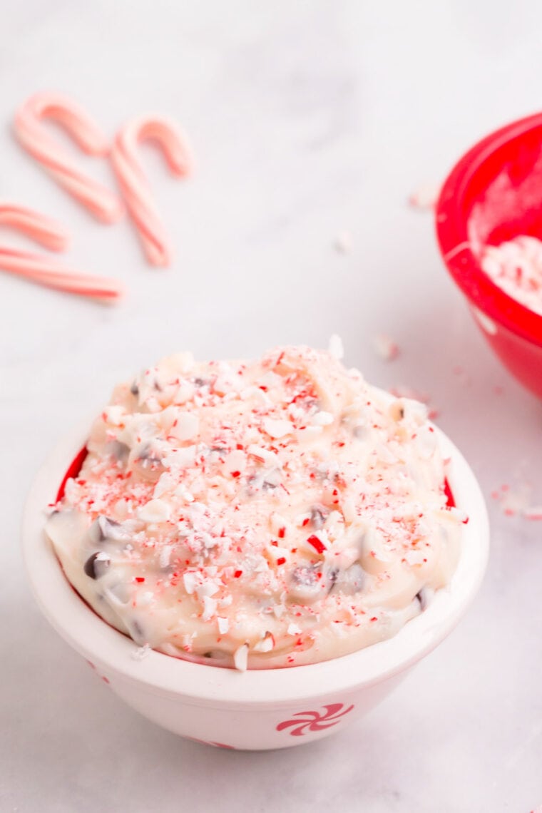Peppermint cheesecake dip topped with crushed candy canes in a white bowl with red holiday design.
