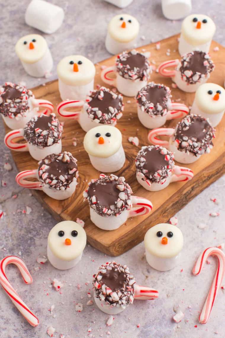 A bunch of chocolate covered marshmallow that look like snowman heads and mugs of peppermint hot cocoa