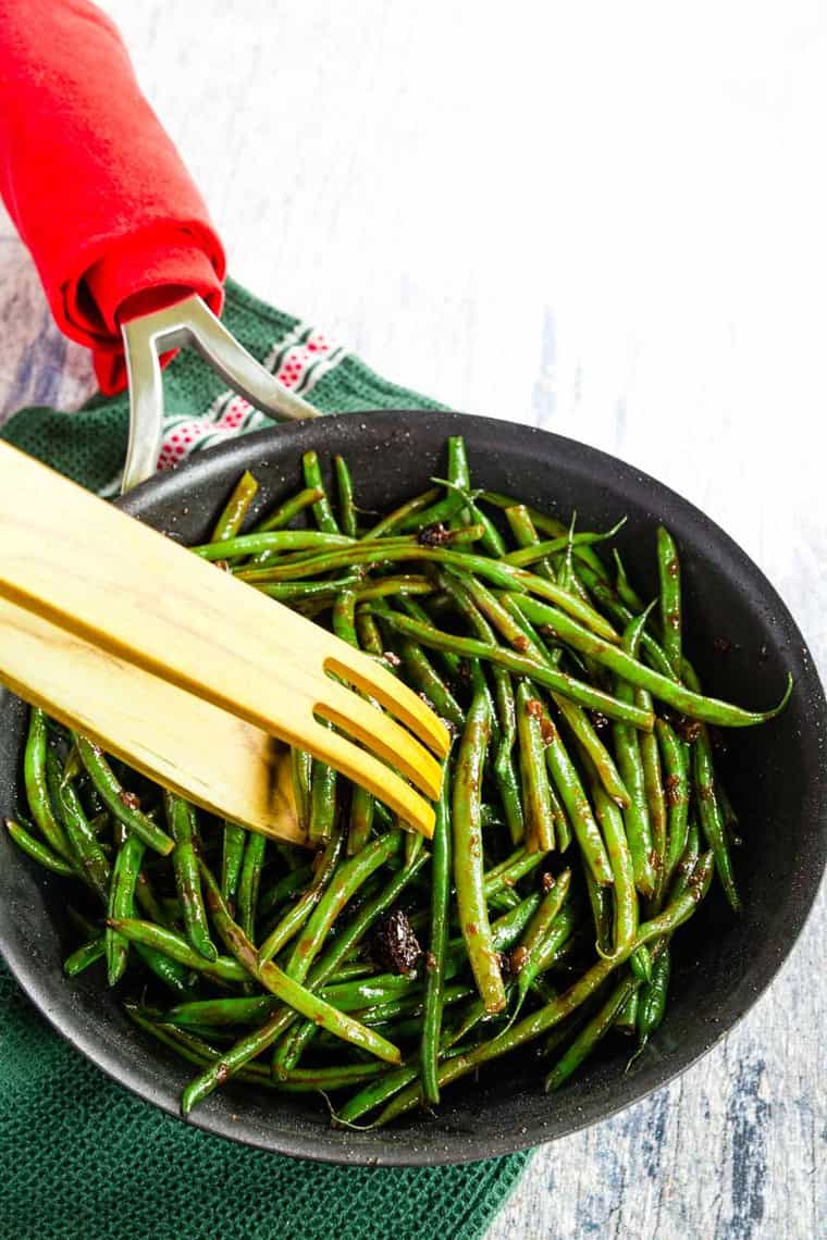 Scooping Balsamic Green Beans out of a skillet with wooden tongs