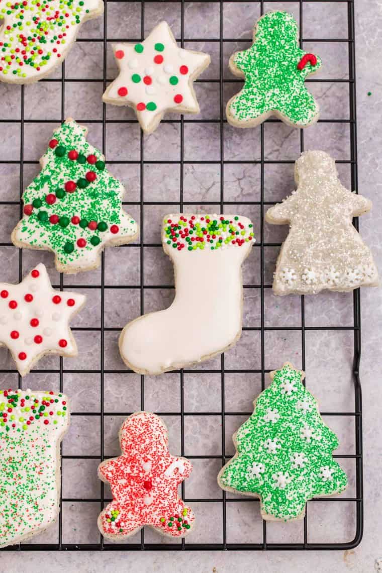 A cooling rach with cut out sugar cookies decorated with frosting and sprinkle sin Christmas colors