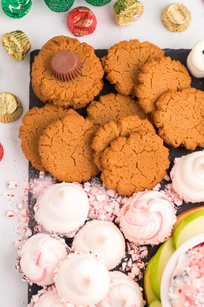 Flourless peanut butter cookies and peppermint meringues on a slate platter with reese's and candy canes in between