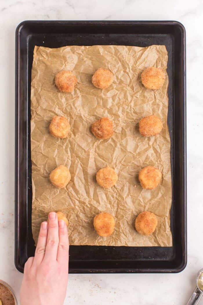 using fingers to press down balls of cookie dough covered in cinnamon sugar