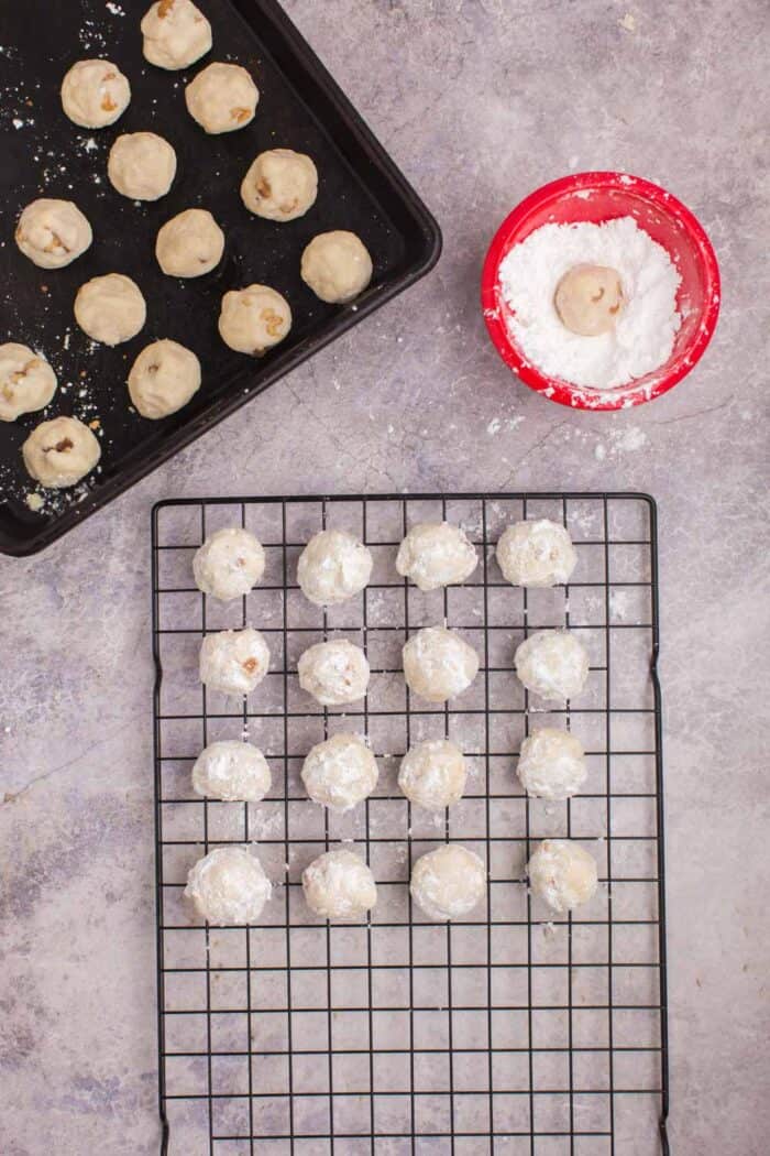 Baked snowball cookies on a rack after being coated with powdered sugar