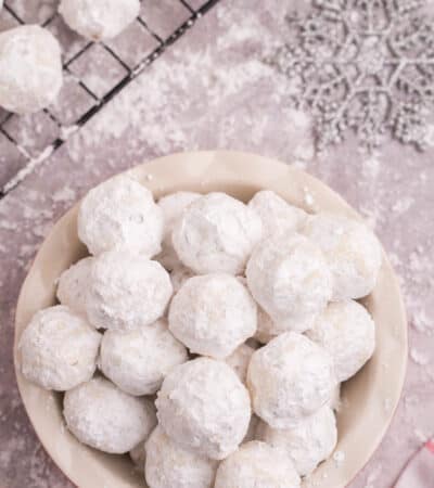 Looking down at a bowl of snowball cookies on a table covered in powdered sugar.