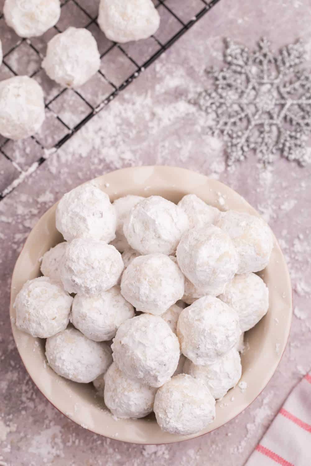 Looking down at a bowl of snowball cookies on a table covered in powdered sugar