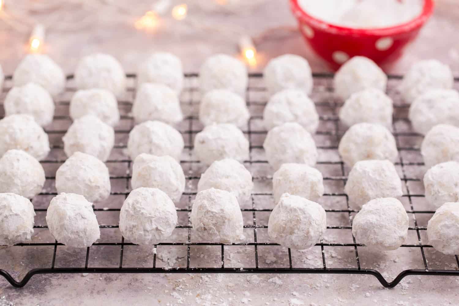 Snowball Cookies on a cooling rack and a red bowl of powdered sugar