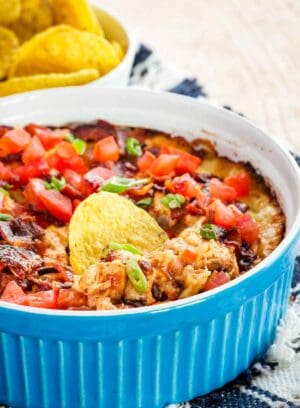 A blue round dish with a cheesy dip and a round tortilla chip in the dip.