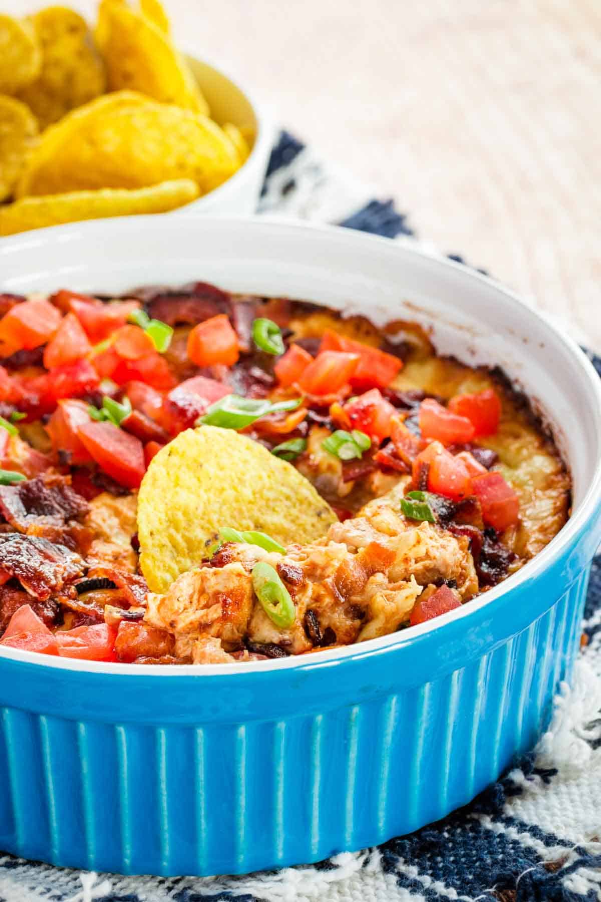 A blue round dish with a cheesy dip and a round tortilla chip in the dip.