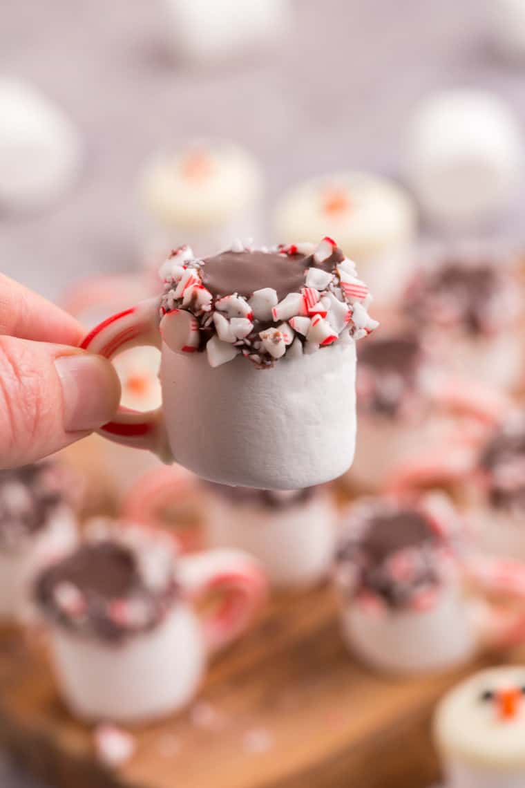 Hand holding a chocolate-covered marshmallow decorated with candy canes to look like a mug of peppermint hot cocoa