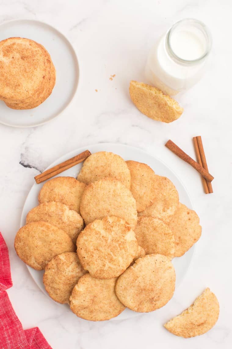 Gluten Free Snickerdoodles spread on a plate with a stack on a smaller plate and a glass of milk