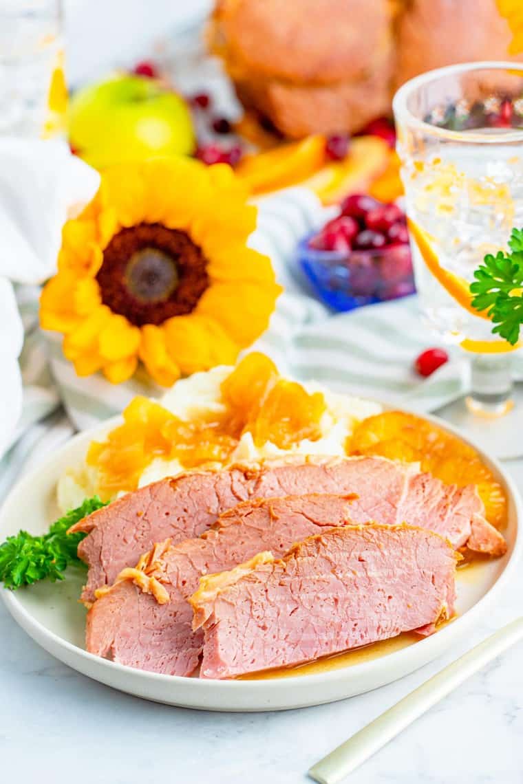 Sliced ham on a plate with mashed potatoes set on a table with a glass of water