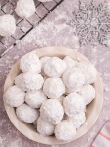 Looking down at a bowl of snowball cookies on a table covered in powdered sugar