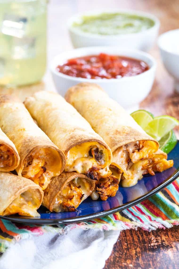 A pile of chicken and black bean taquitos on a plate with cheede oozing out