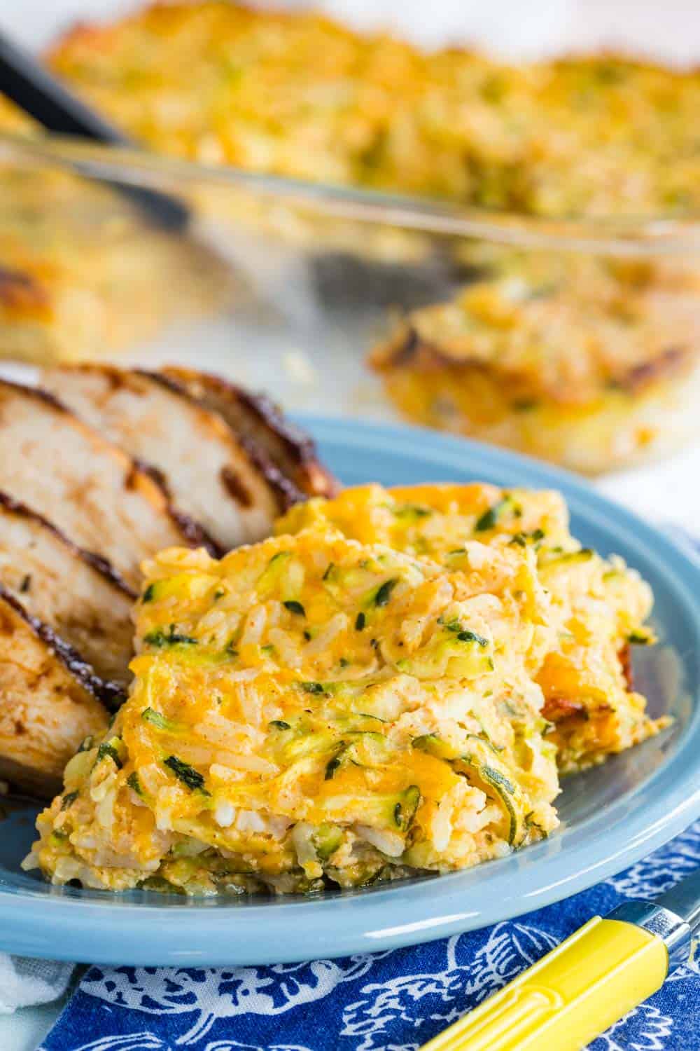 Two squares of cheesy zucchini rice casserole on a plate with some chicken.