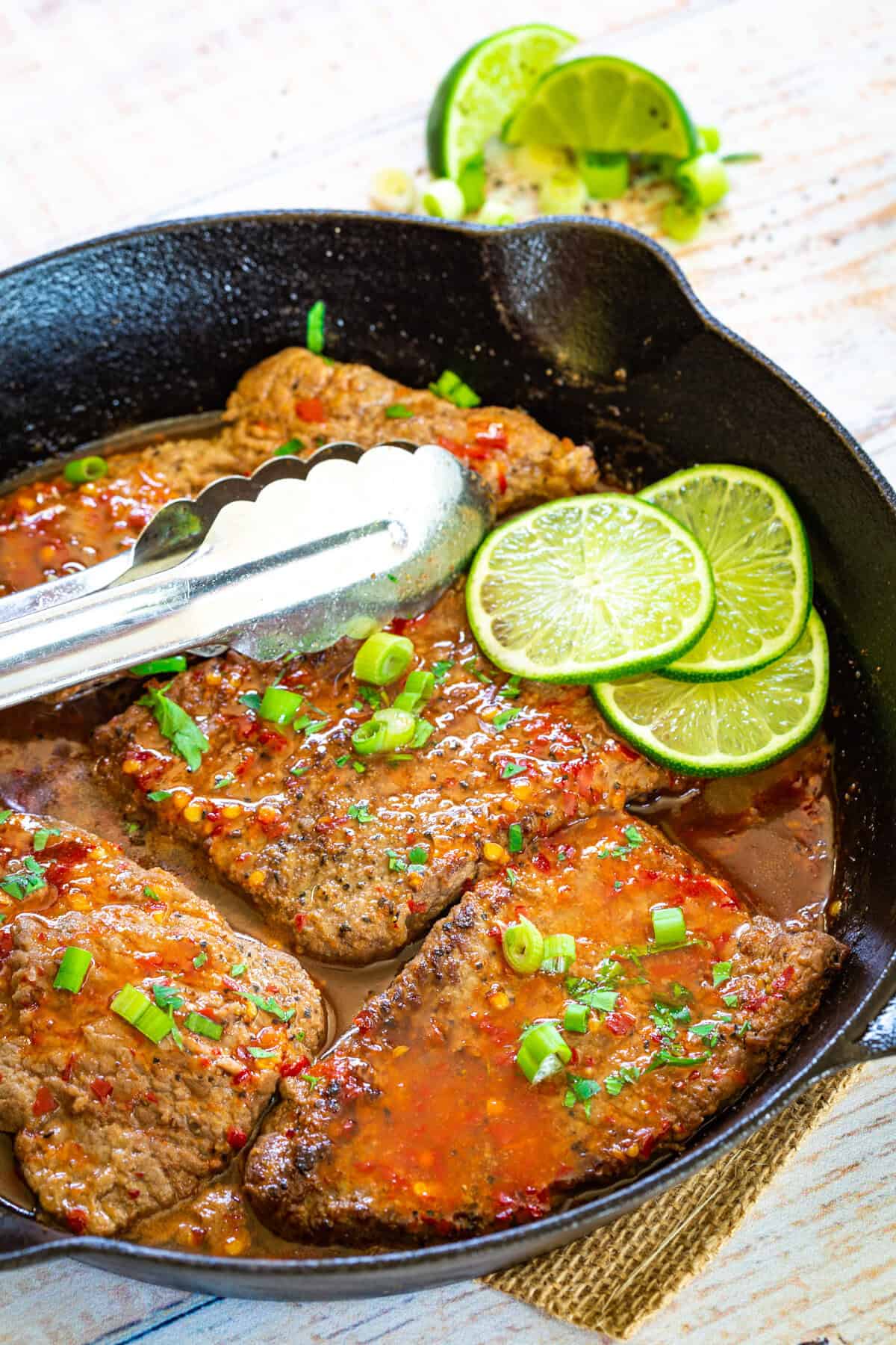 Tongs on a pan of chili lime cube steaks