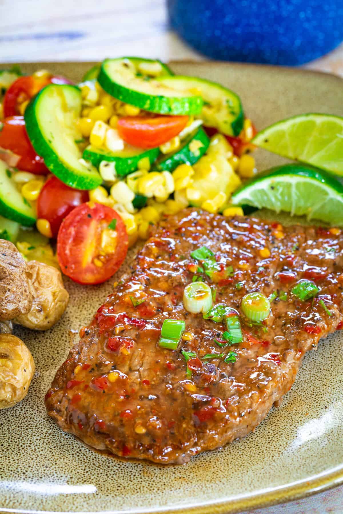 Pan seared cube steaks on a plate with sauteed summer veggies