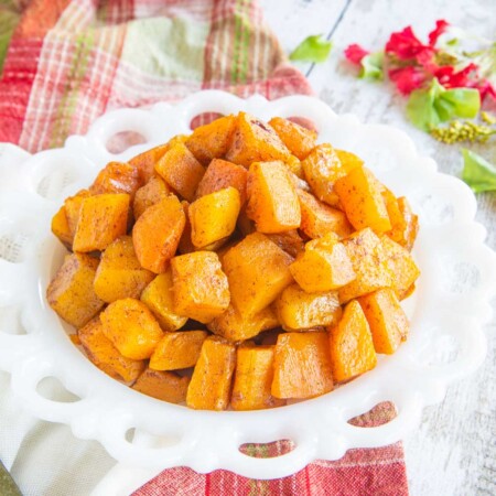 white plate with a pile of cinnamon roasted butternut squash with a serving spoon next to it