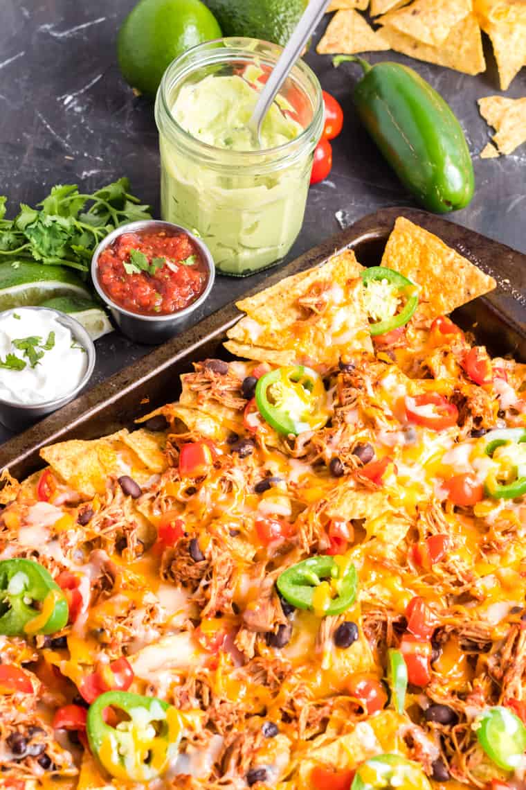 Chicken nachos on a sheet pan with small bowls of salsa, sour cream and avocado cream