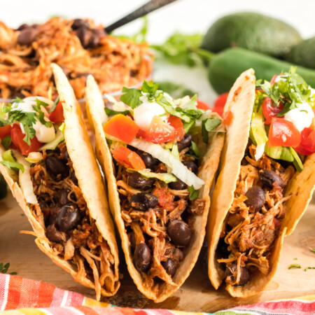 Three chicken tacos standing up on a cutting board