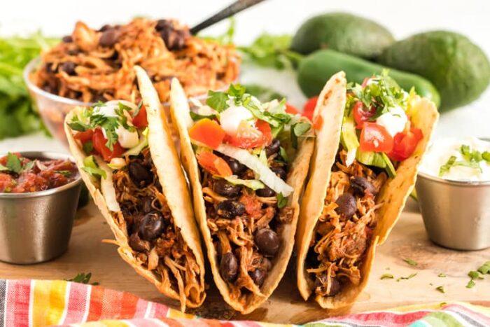 Three chicken tacos standing up on a cutting board