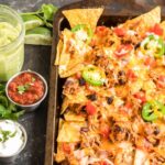 Sheet pan chicken nachos with bowls of toppings on the side