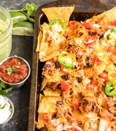 Sheet pan chicken nachos with bowls of toppings on the side