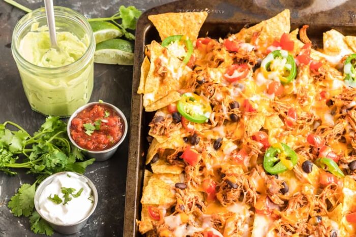 Sheet pan chicken nachos with bowls of toppings on the side