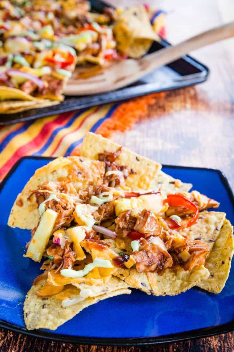 Tortilla chips covered with chicken, bbq sauce, cheese, and toppings on a blue plate.