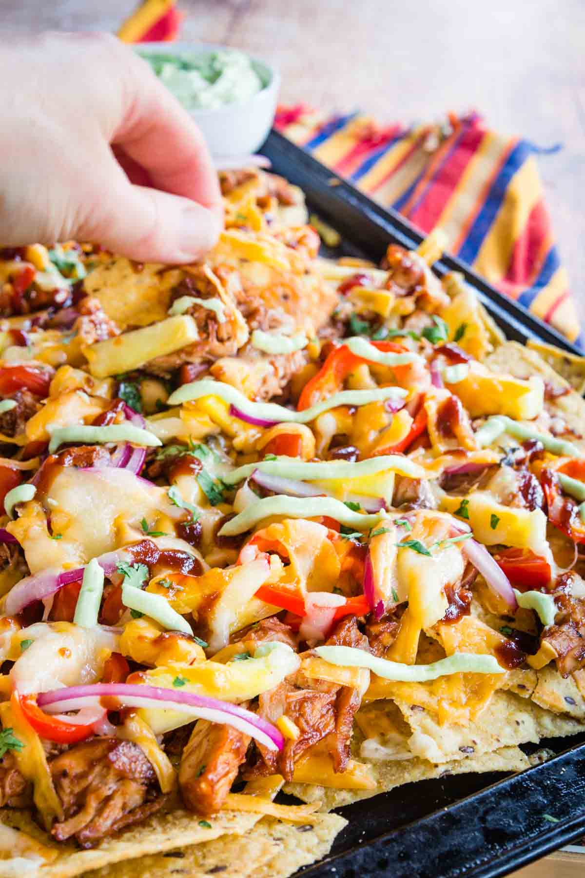 A hand picking up one of the barbecue chicken nachos from the baking sheet.