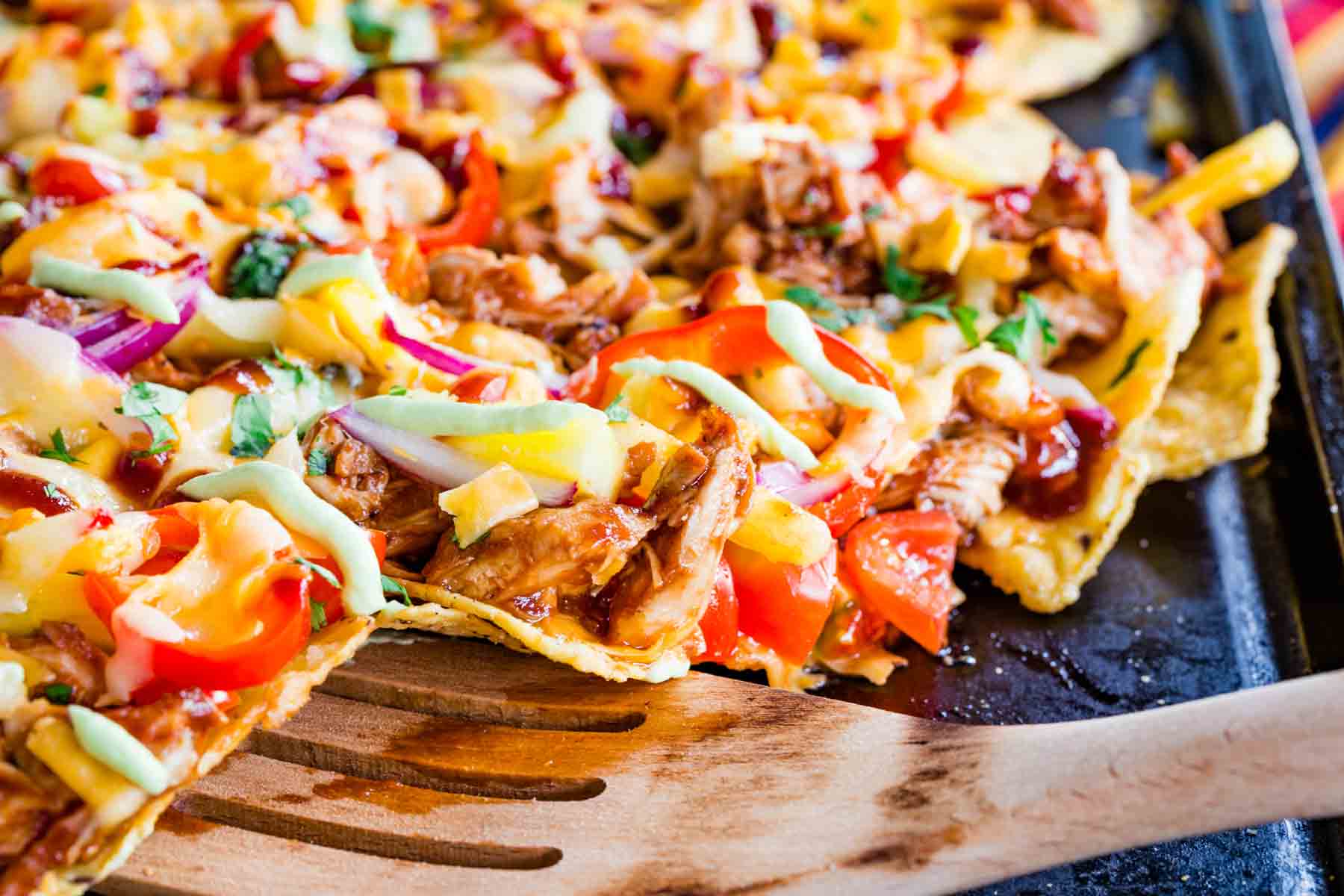 A wooden spatula picking up some of the nachos on a sheet pan.