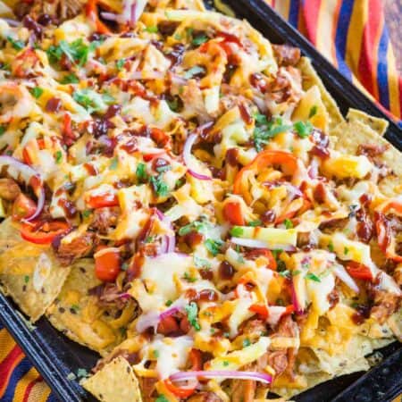 Barbeque chicken nachos cooked on a baking sheet on top of a striped cloth napkin.