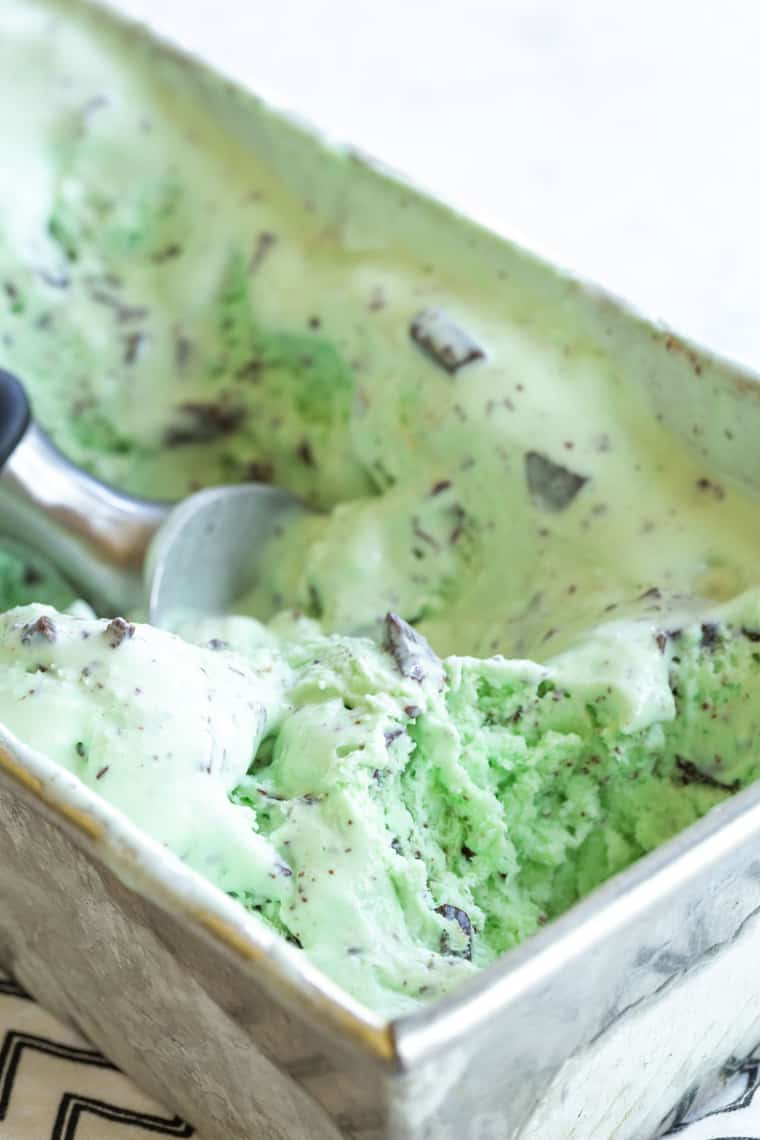 A batch of Mint chocolate chip ice cream in a metal loaf pan with a scoop