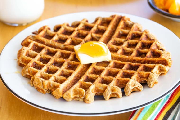 Golden brown waffle on a plate with a pat of butter and syrup