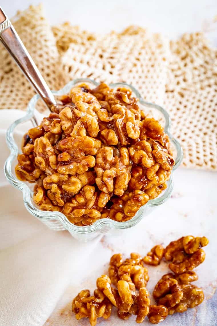 bowl of honey glazed walnuts with some laying on the table