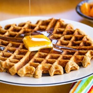 A banana waffle on a white plate with a blue edge with butter and syrup on top.