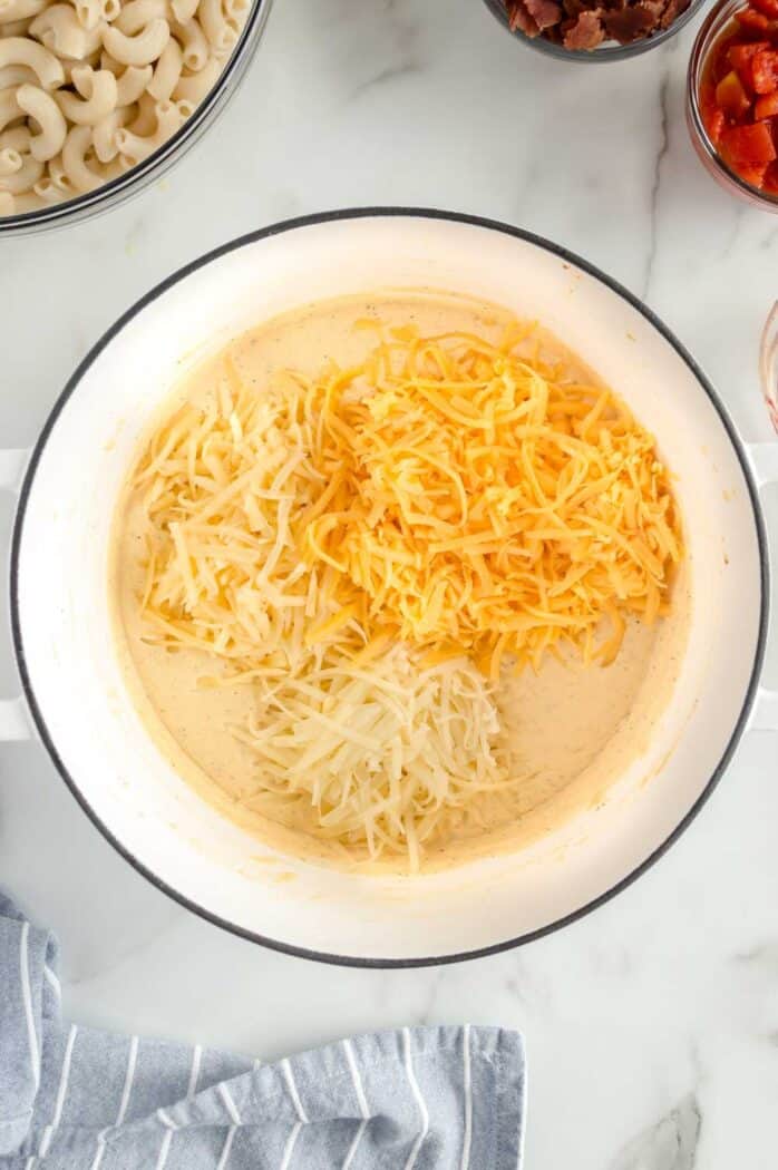 three kinds of shredded cheese added to the cream sauce in the pot