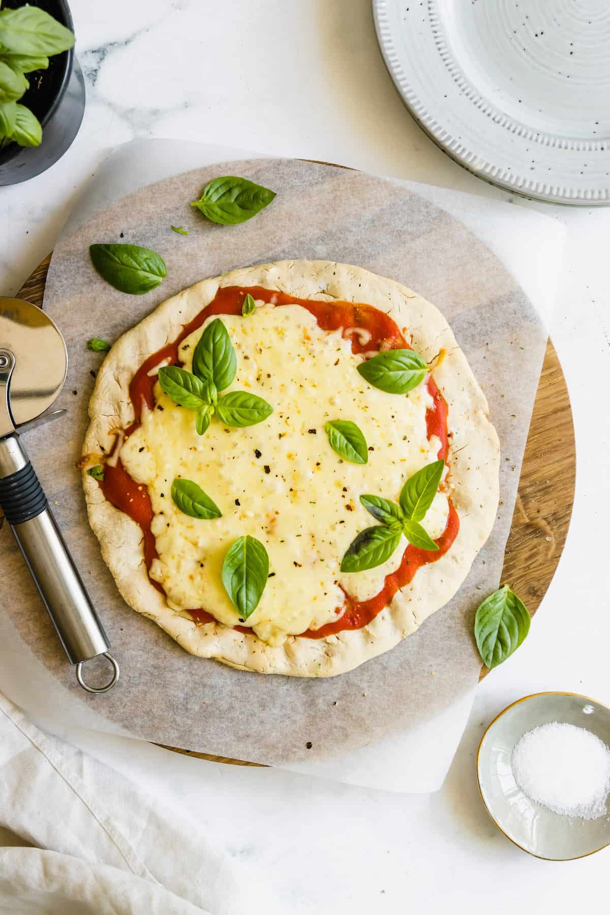 A Pizza Stone Holding a Cheesy Pizza with Gluten-Free Crust and a Pizza Cutter