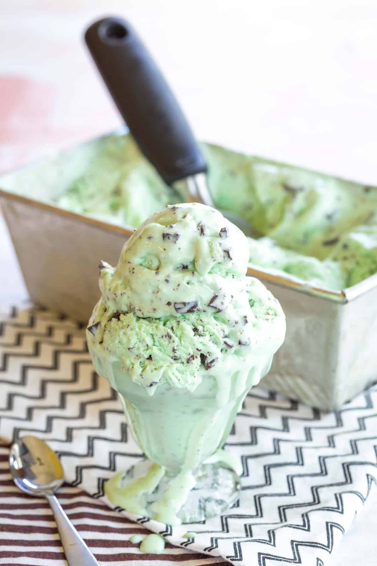 A dish of homemade mint chocolate chip ice cream with the loaf pan of ice cream behind it