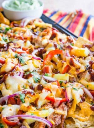 A closeup of nachos topped with chicken, cheese, red onions, and avocado cream.