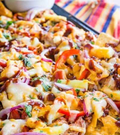 A closeup of nachos topped with chicken, cheese, red onions, and avocado cream.