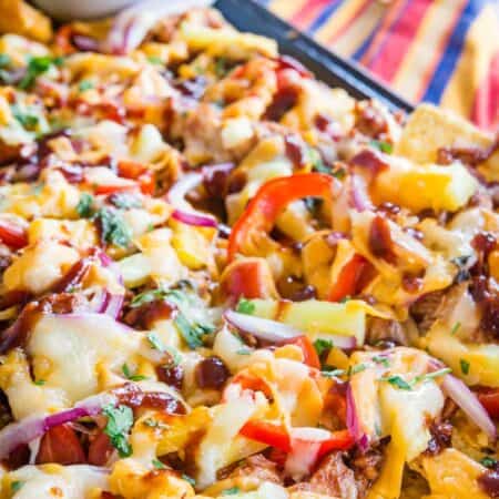 A closeup of nachos topped with chicken, cheese, red onions, and avocado cream.
