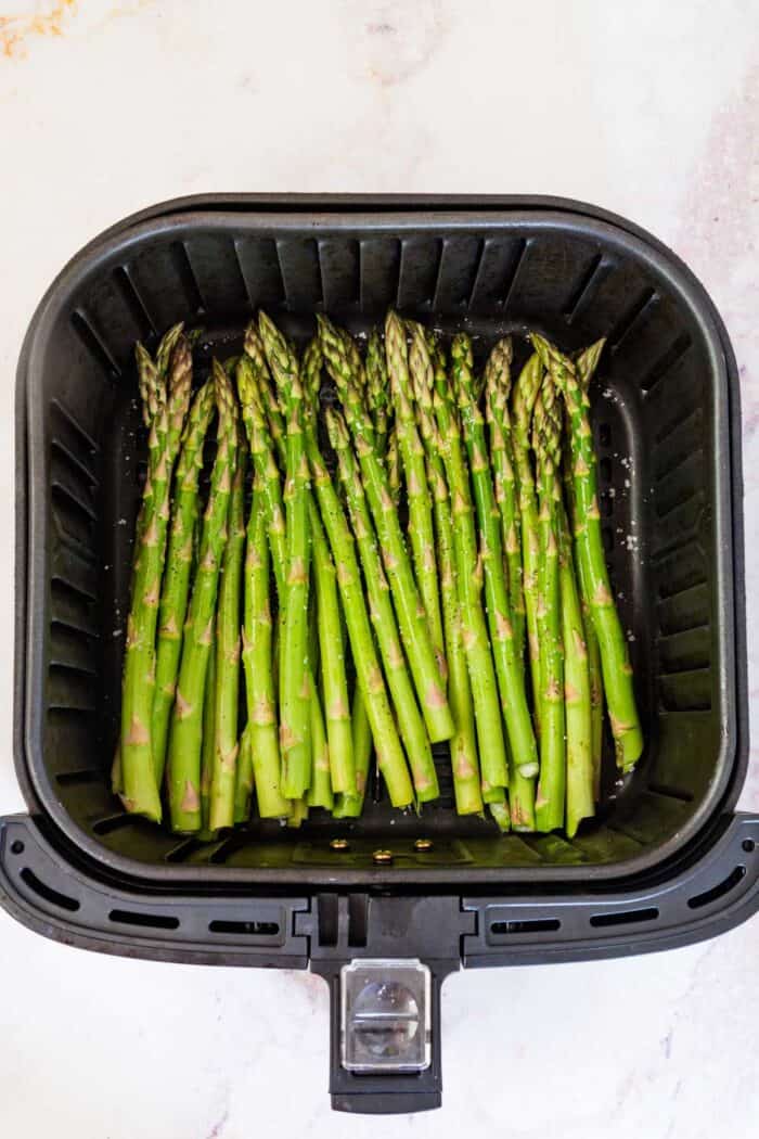 raw asparagus seasoned with salt and pepper in an air fryer basket